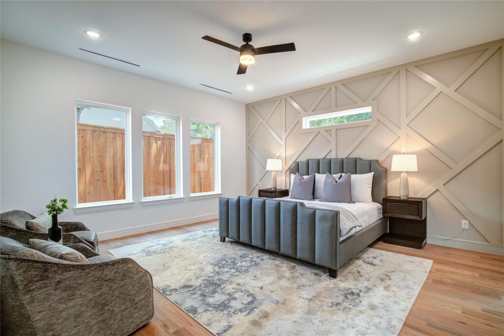 Modern bedroom with large windows and gray upholstered bed.