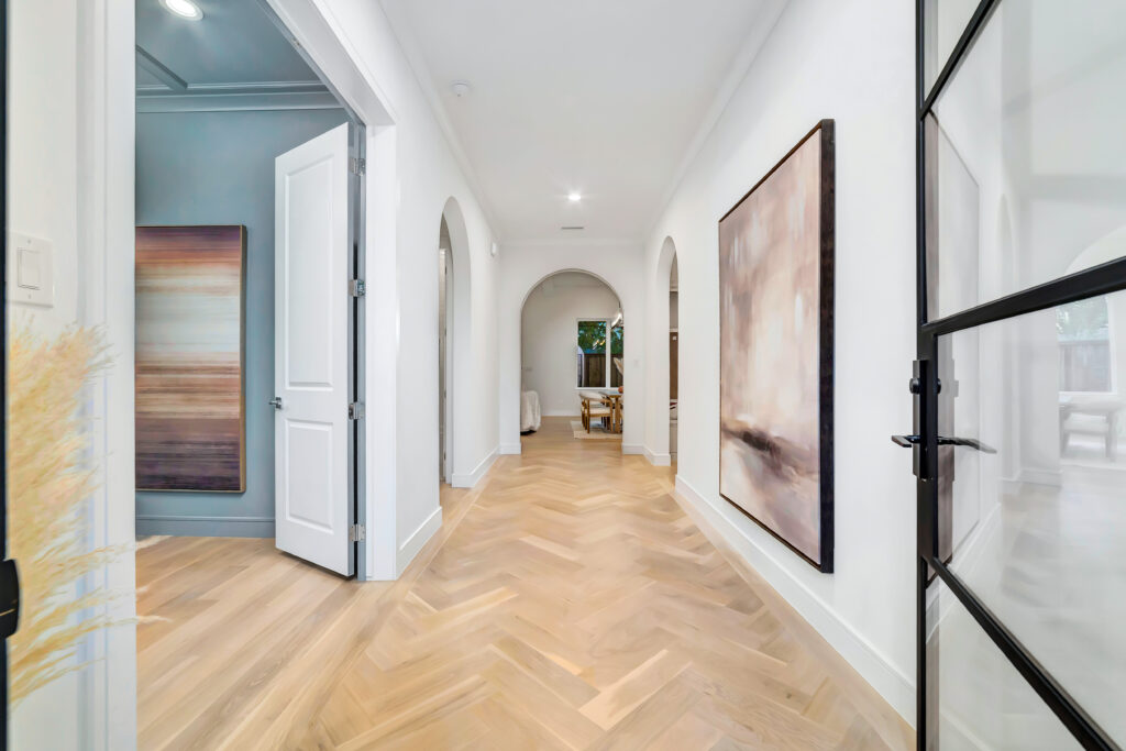 Bright hallway with wooden herringbone floor and large wall art.