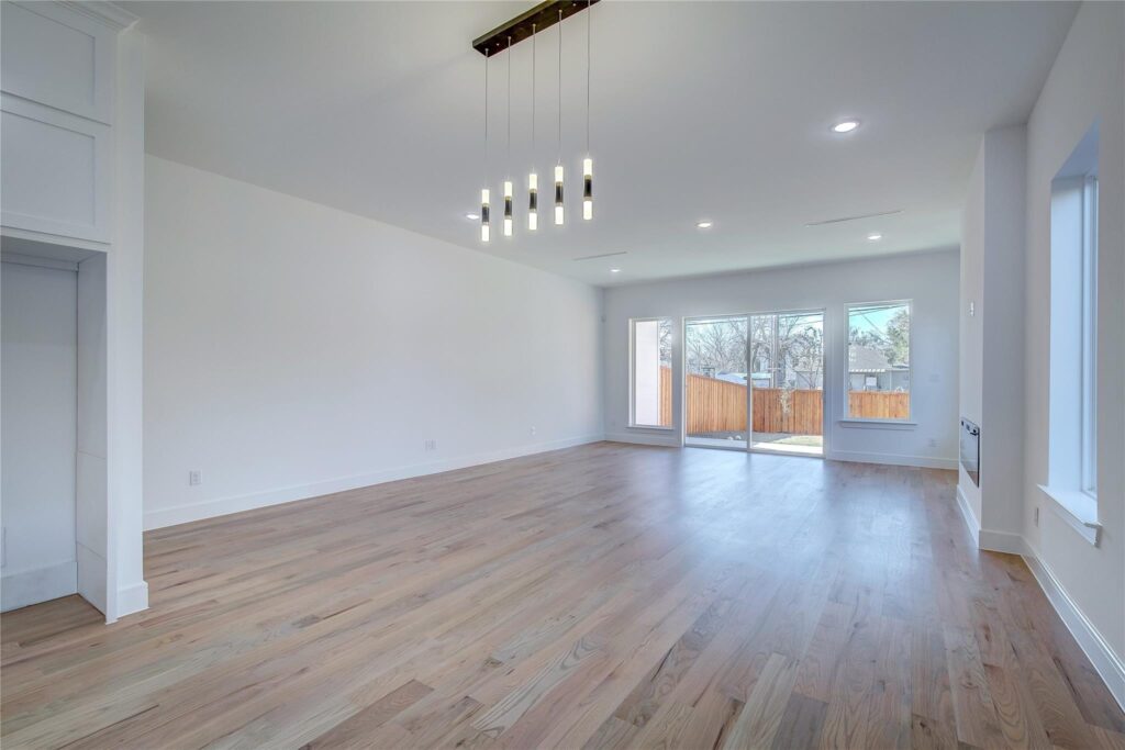 Spacious empty living room with wooden floors and modern lighting.
