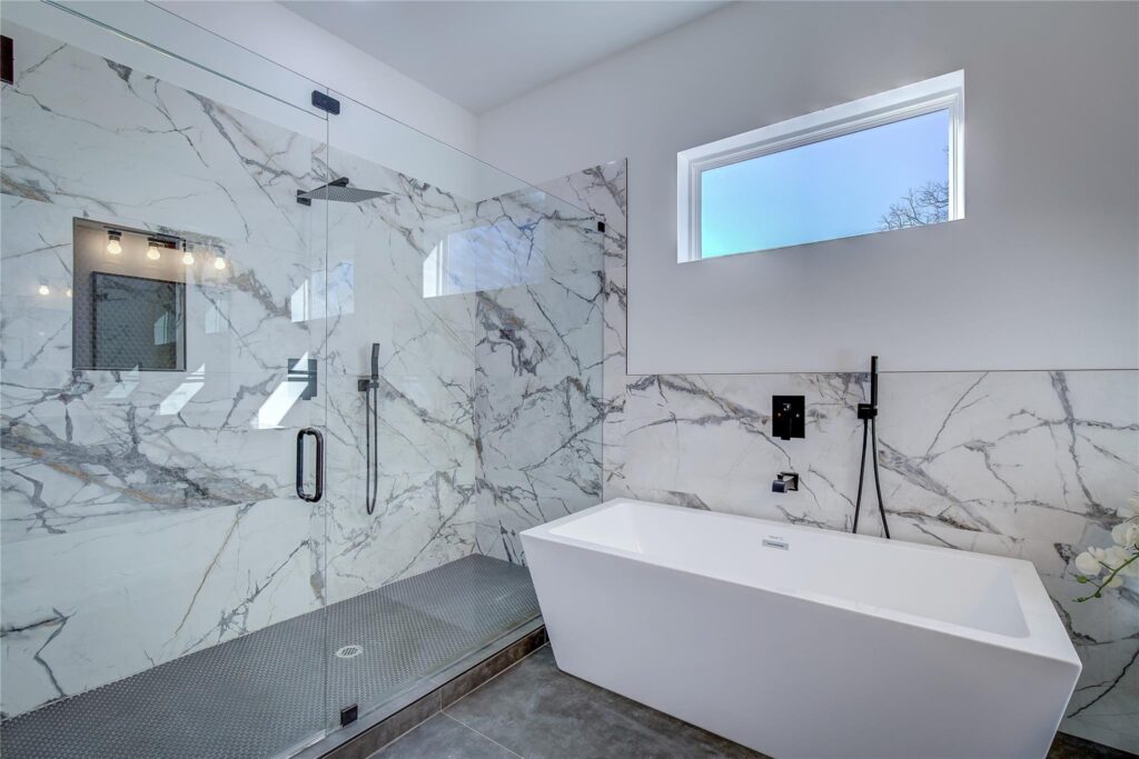 Modern bathroom with marble walls, a glass shower, and a freestanding bathtub.