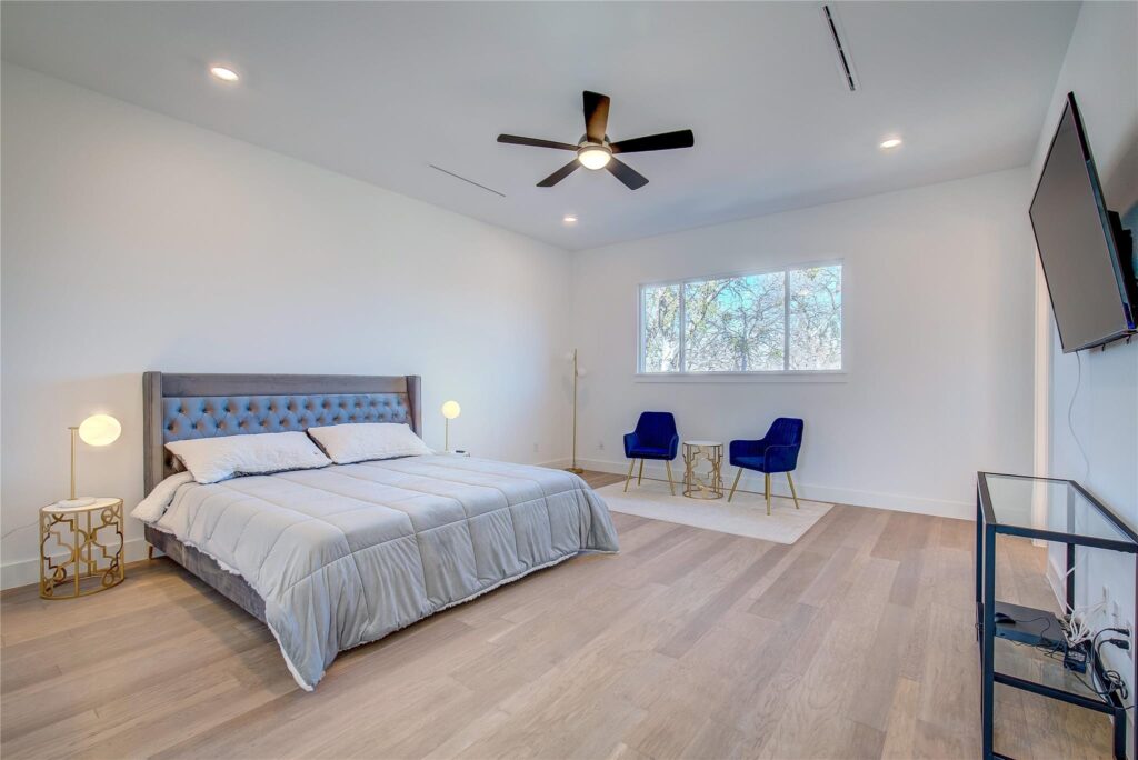 Modern bedroom with a large bed, ceiling fan, and two blue chairs by the window.