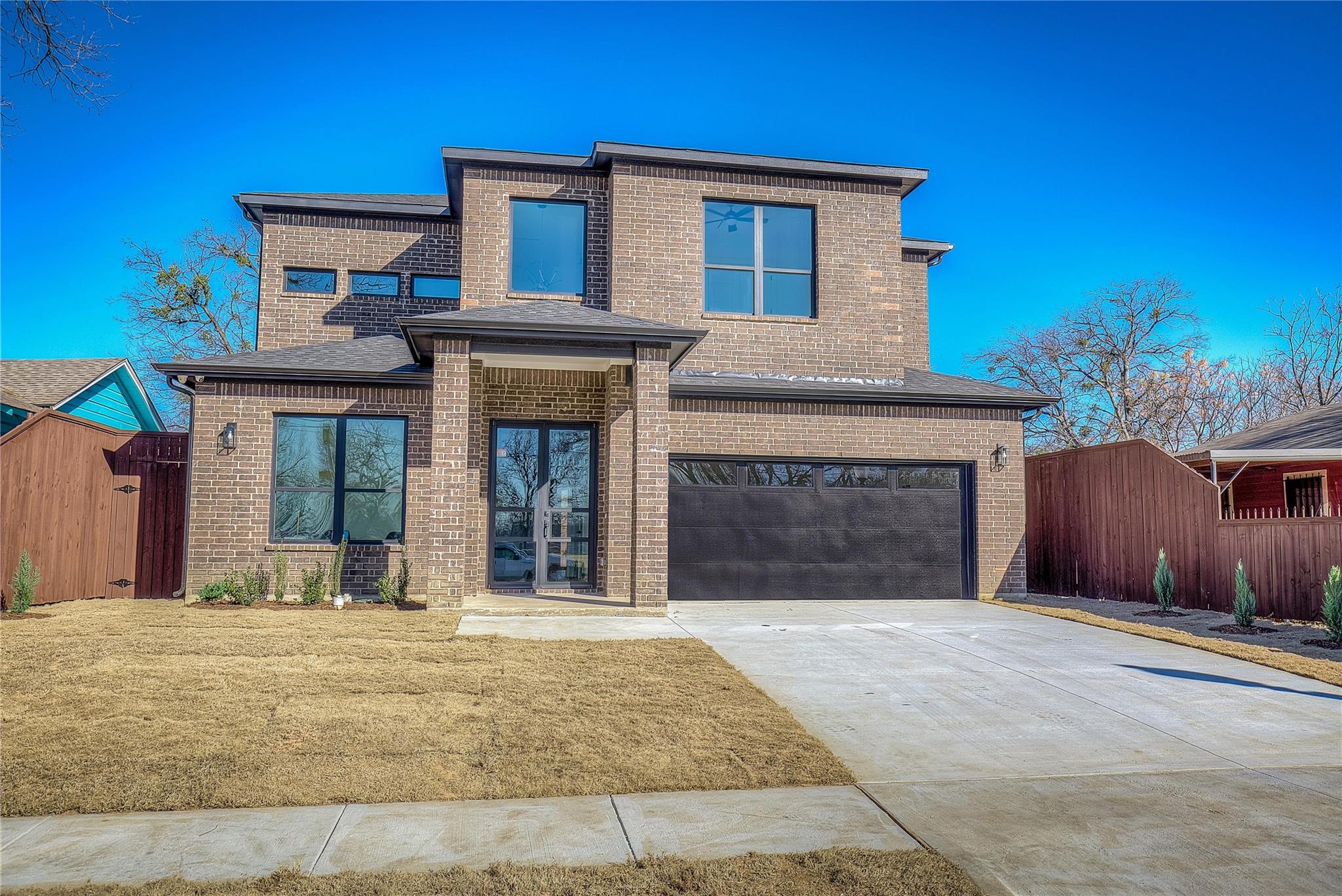 A modern two-story brick house with a double garage and clear blue sky.