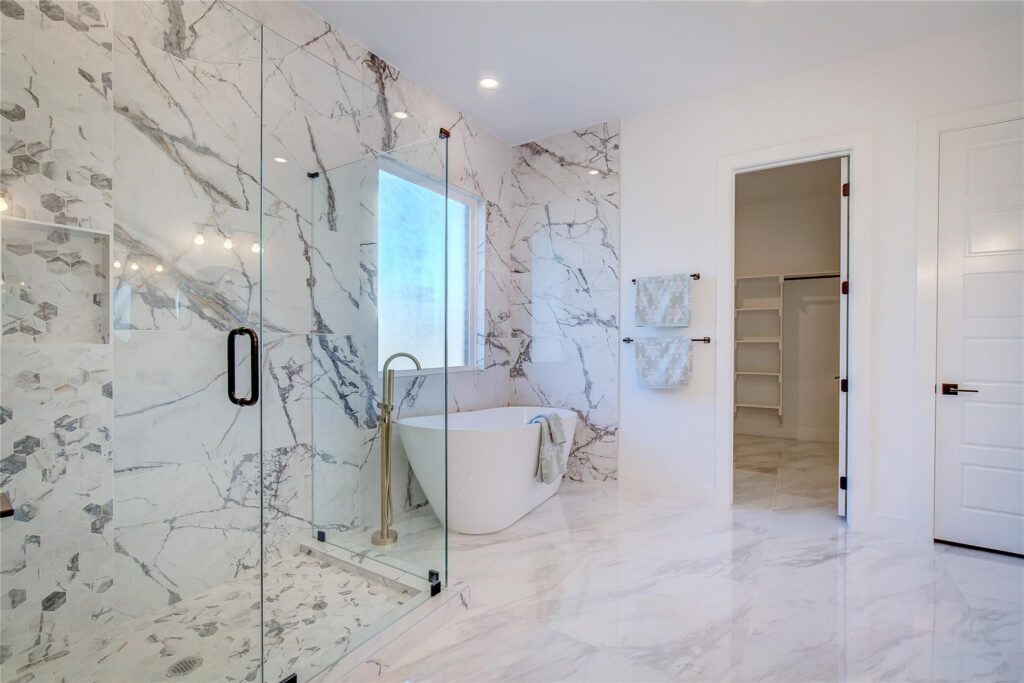 Modern bathroom with marble walls, freestanding tub, and glass shower enclosure.