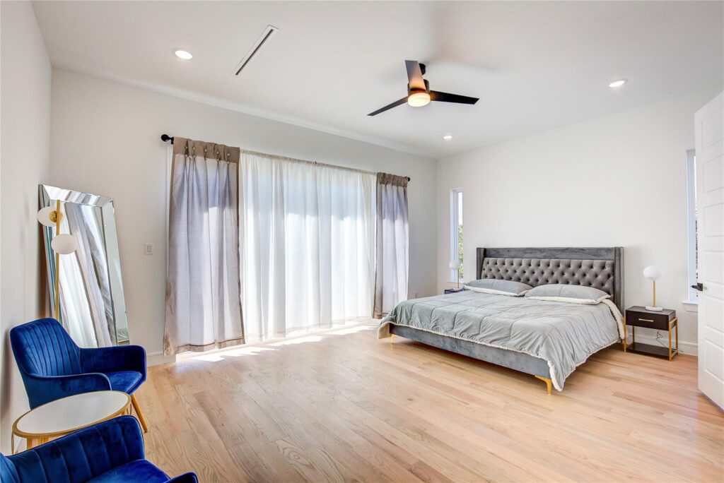 Bright, modern bedroom with wooden floors and a large window with sheer curtains.