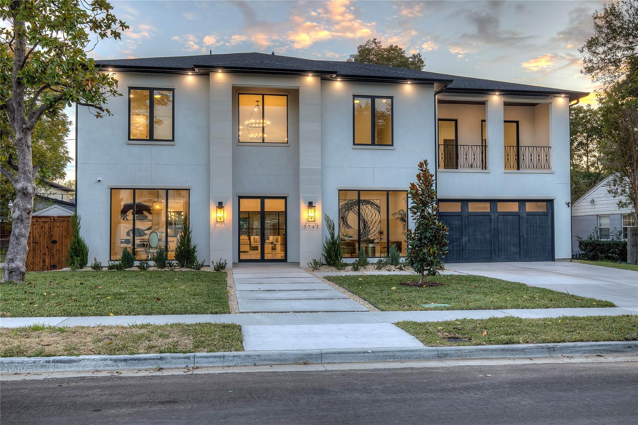 Modern two-story house with large windows and warm interior lighting at dusk.