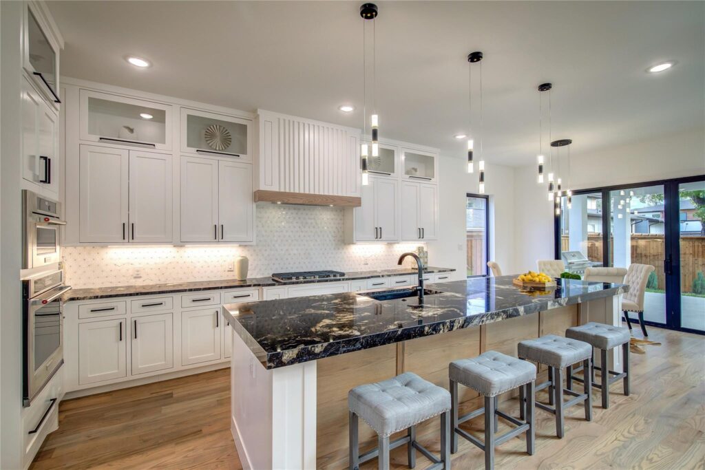 Modern kitchen with marble island and pendant lights.