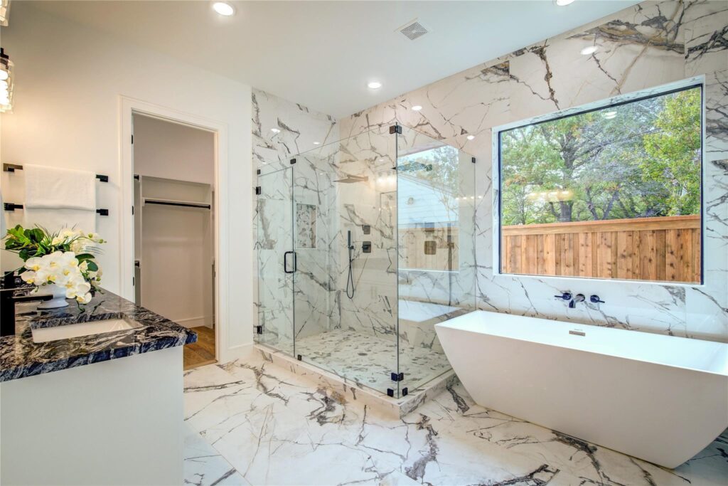 Modern bathroom with glass shower, freestanding tub, and marble floors.